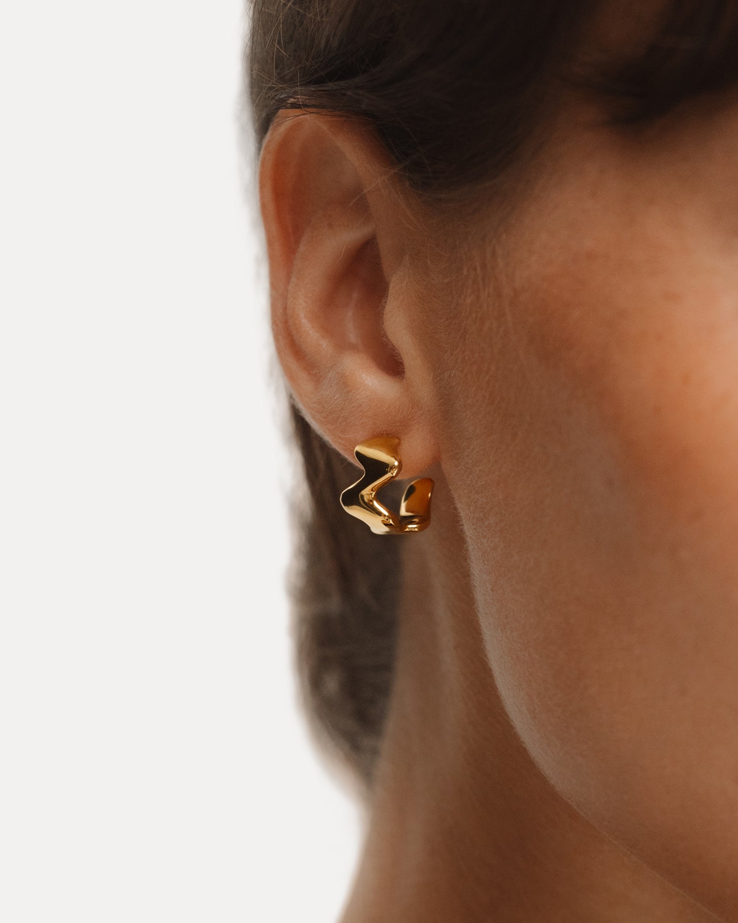 The POISE Huggie Hoops in 18k Gold Vermeil shown on the ear of a model - NATALIE GRASSI